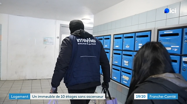 Capture d'écran d'un reportage publié par France 3 au sujet d'un immeuble en panne d'ascenseur à Besançon. On voit sur cette image un des salariés d'INTERMED aider une résidente à porter ses courses.
